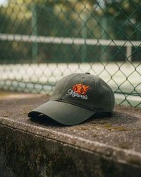 Green cap with a logo on a concrete surface with a chain-link fence and tennis court in the background