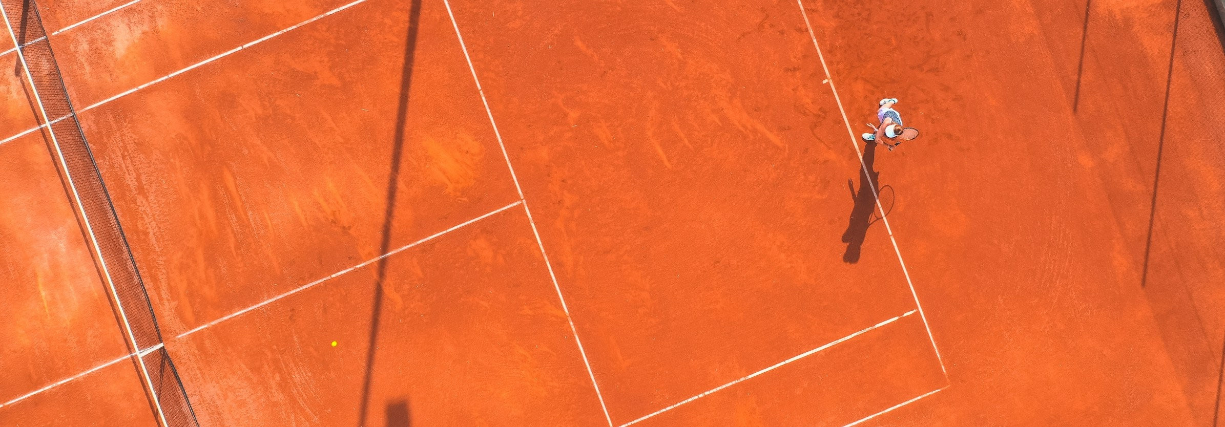 Tennis player on a red clay court from an aerial perspective