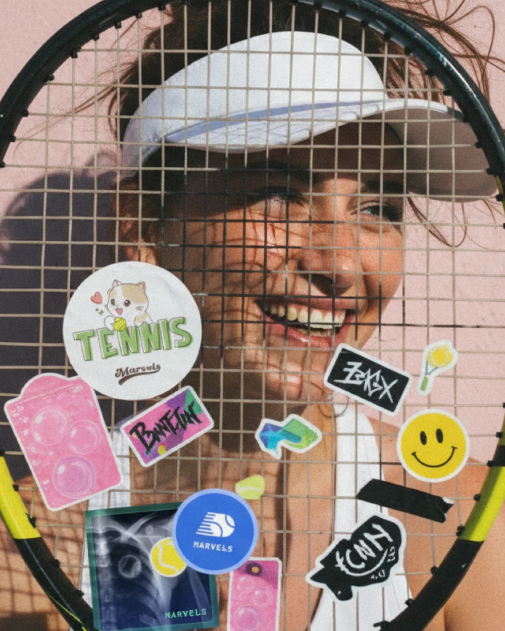 Person holding a tennis racket with various stickers on a pink wall background