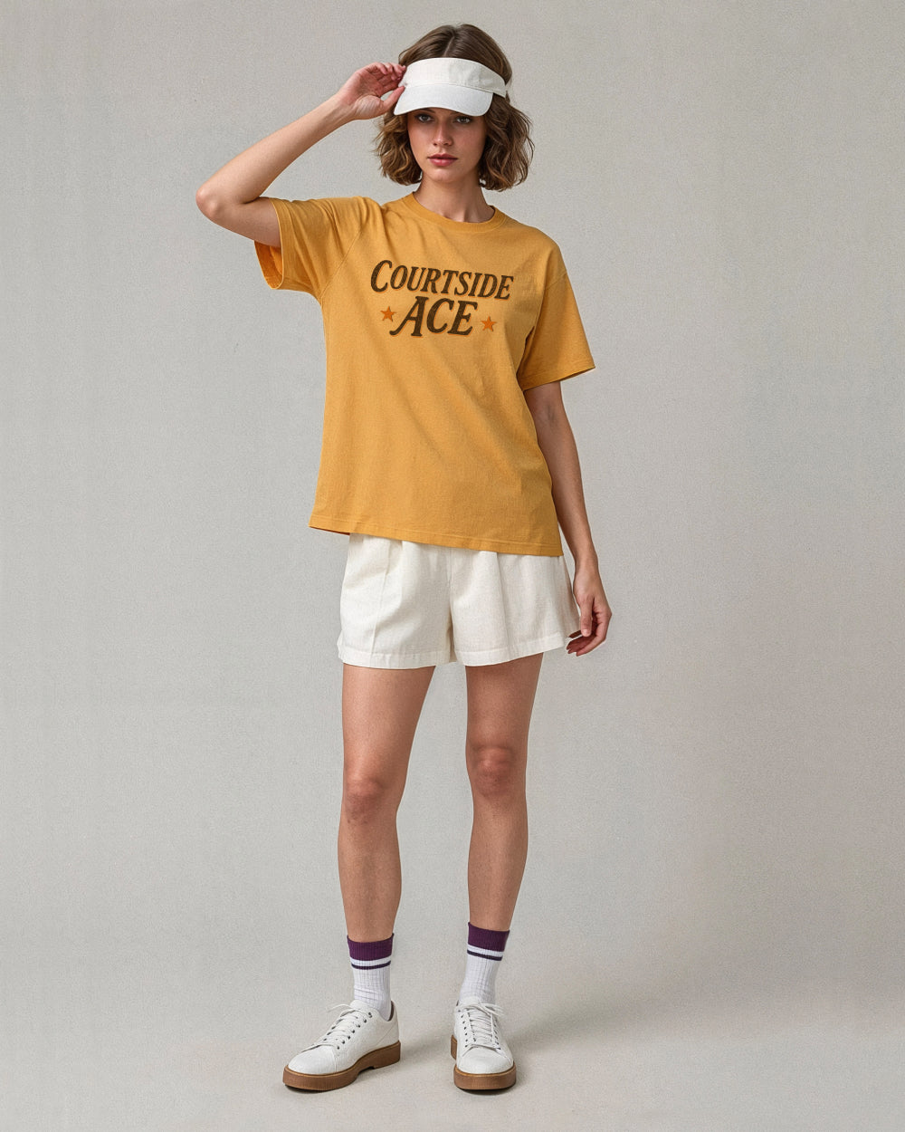 Person wearing a yellow gold 'Courtside Ace' t-shirt with white shorts on a plain background