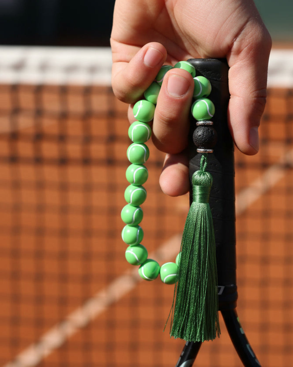 Green tennis beaded tespih with tassel held by a hand on a tennis court background