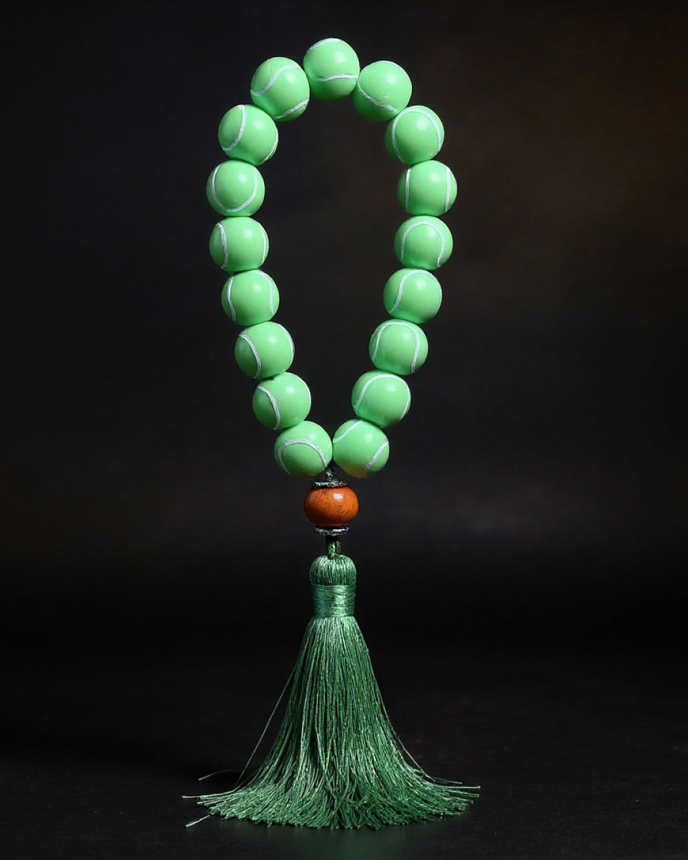 Green tennis ball prayer beads with a tassel on a black background