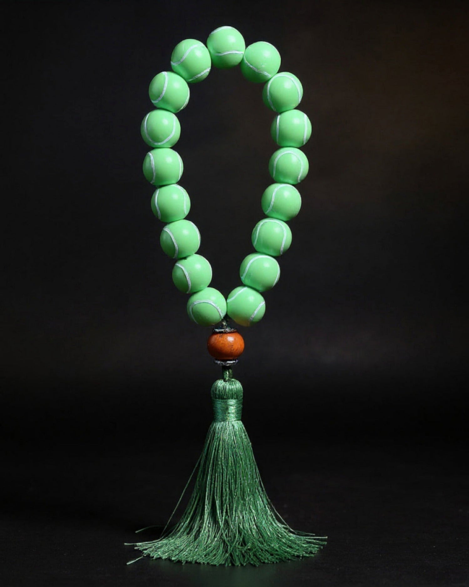 Green tennis ball prayer beads with a tassel on a black background