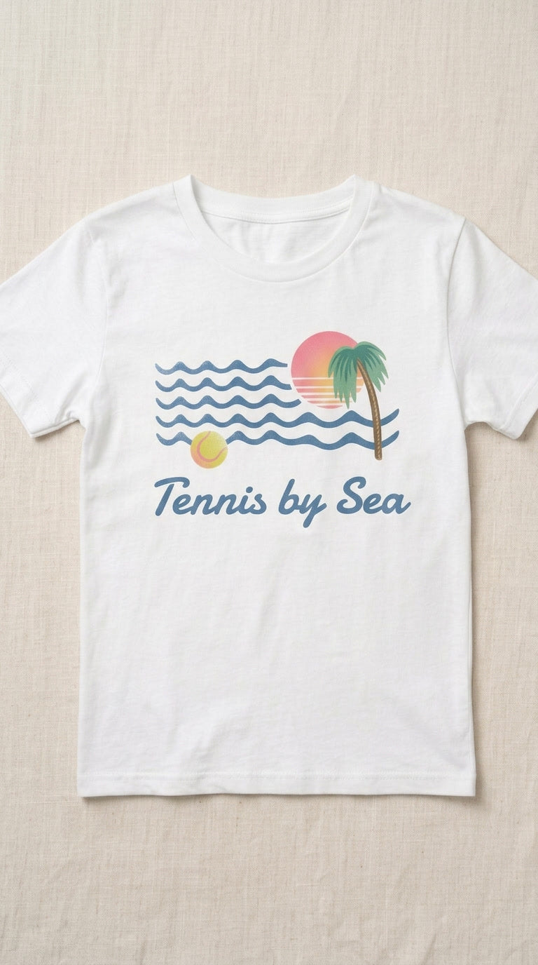 A white short-sleeve crewneck t-shirt laid flat on a light beige textured fabric background. The shirt features a retro graphic of blue ocean waves, a yellow sun, a pink and orange sunset, a green palm tree, and the text 'Tennis by Sea' in blue script.