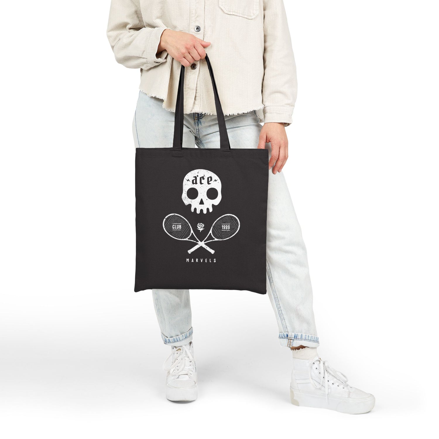 Person holding a black tote bag with a skull and tennis graphic on a white background