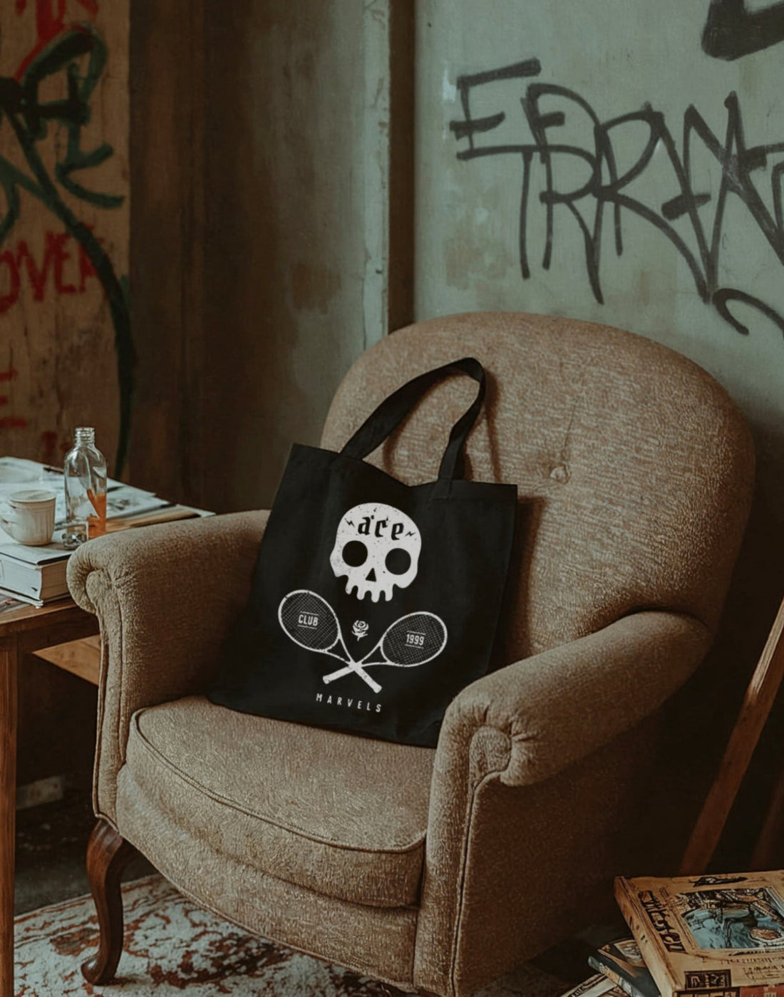 Black tote bag with skull and tennis racket design on a brown armchair in a room with graffiti.