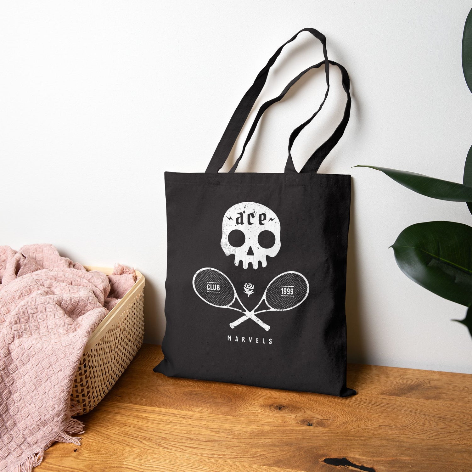 Black tote bag with white skull tennis graphic design on a wooden surface
