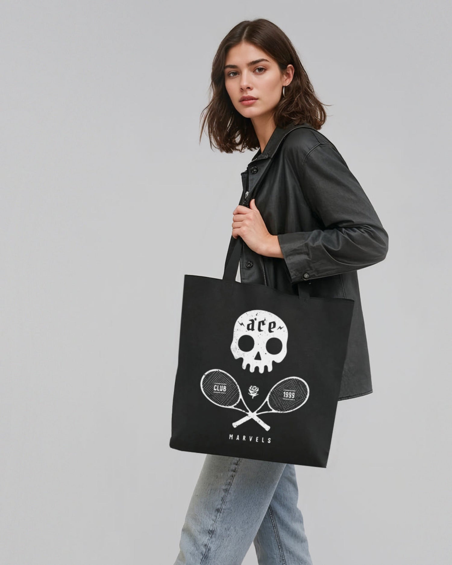 Woman holding a black tote bag with a skull and crossbones design on a gray background