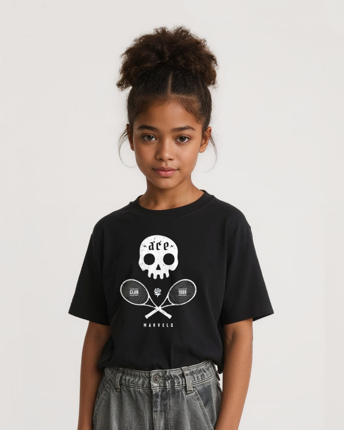 Young girl wearing a black t-shirt with a white  skull and crossed tennis rackets graphic design on a plain background