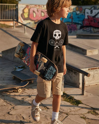 Child holding a skateboard in a skate park with graffiti in the background