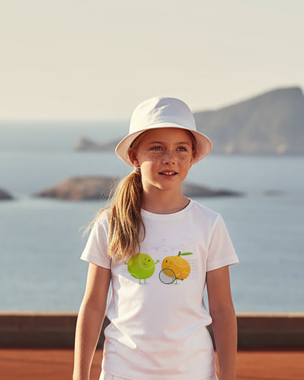 Young girl wearing a white t-shirt with a tennis graphic design by the sea