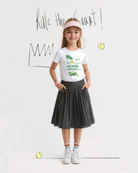 Young girl in sports attire with 'Good Serves' t-shirt and tennis-themed background