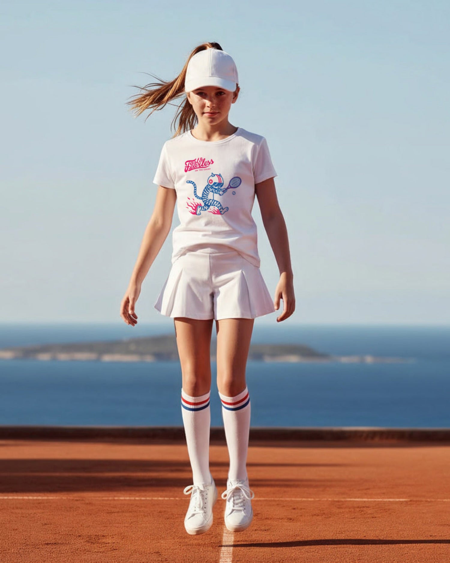 Young girl wearing a white t-shirt with a tennis design on a seaside background