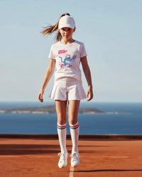 Young girl wearing a white t-shirt with a tennis design on a seaside background