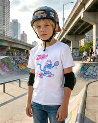 Boy at a skateboard park wearing a helmet and a white t-shirt with a tennis graphic