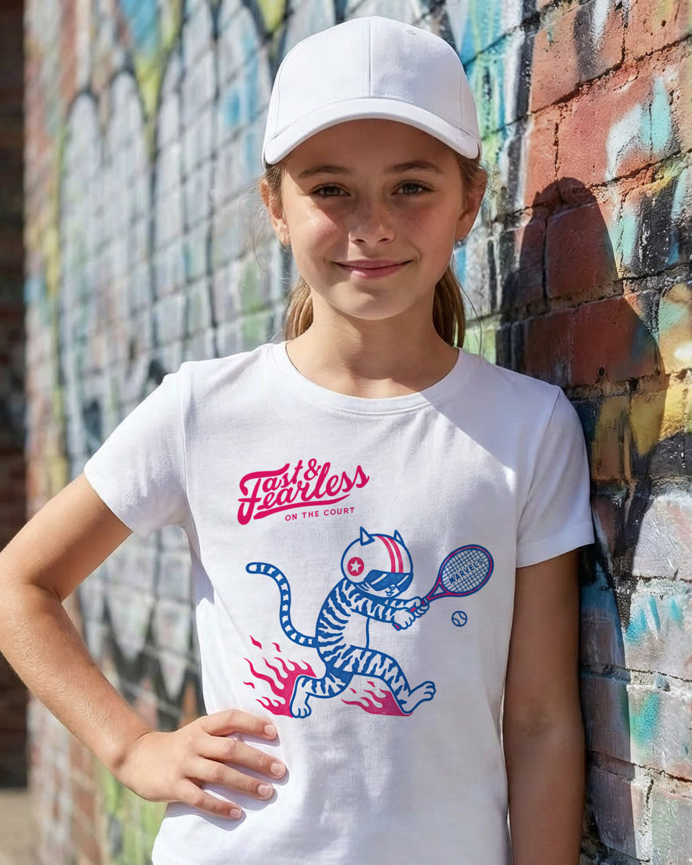 Young girl wearing a white t-shirt with a tennis graphic design, standing against a colorful mural.