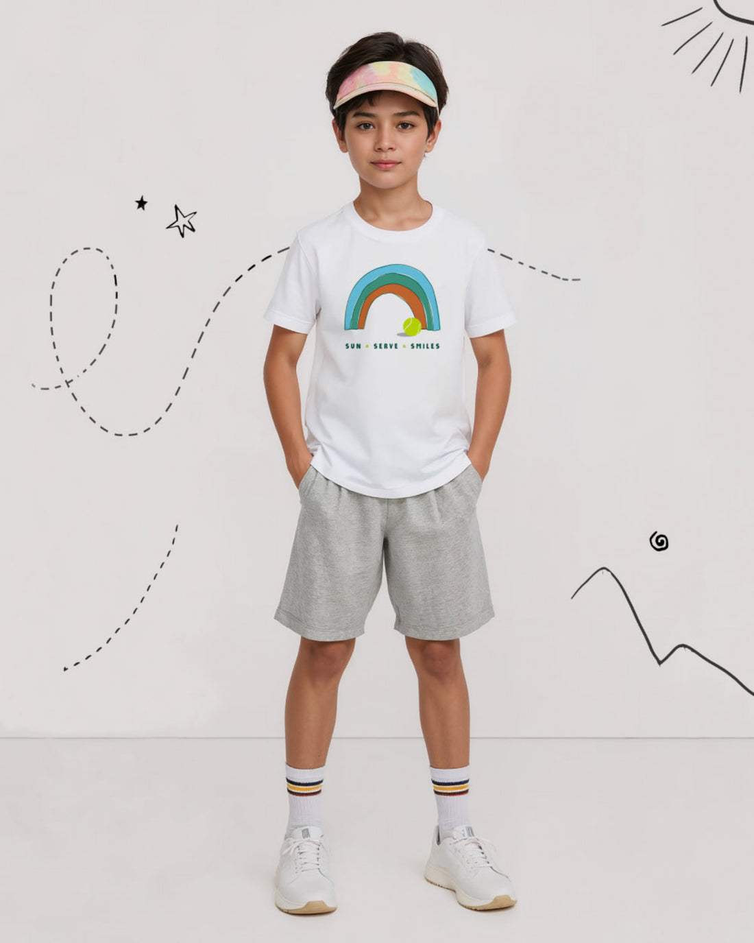 Child wearing a white tennis t-shirt with a rainbow design, gray shorts, and white sneakers on a white background.