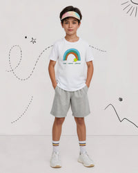 Child wearing a white tennis t-shirt with a rainbow design, gray shorts, and white sneakers on a white background.