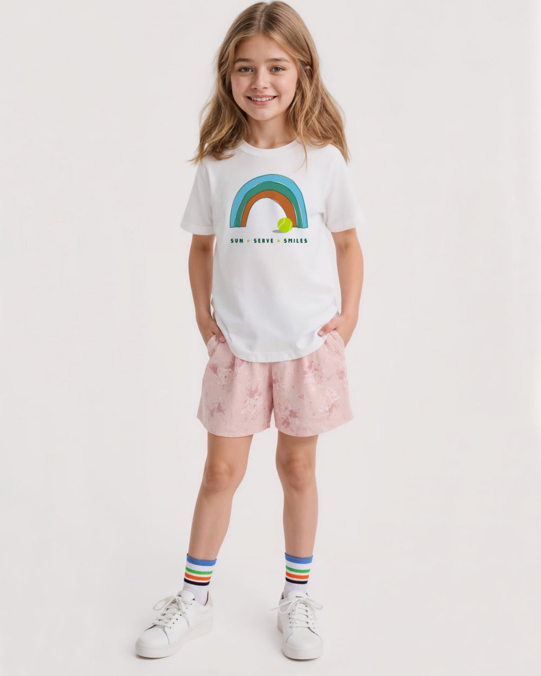 Young girl wearing a white t-shirt with a rainbow design and pink shorts on a white background