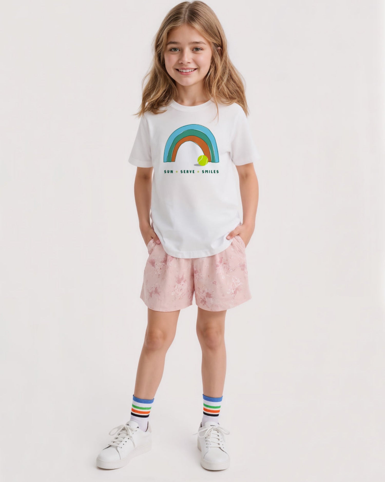 Young girl wearing a white t-shirt with a rainbow design and pink shorts on a white background