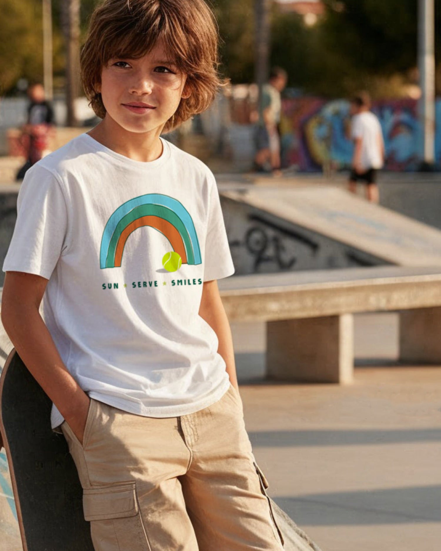 Child wearing a white tennis t-shirt with a rainbow design at a skate park.