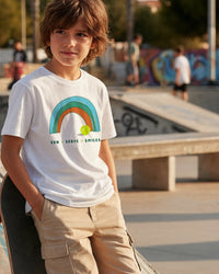 Child wearing a white tennis t-shirt with a rainbow design at a skate park.