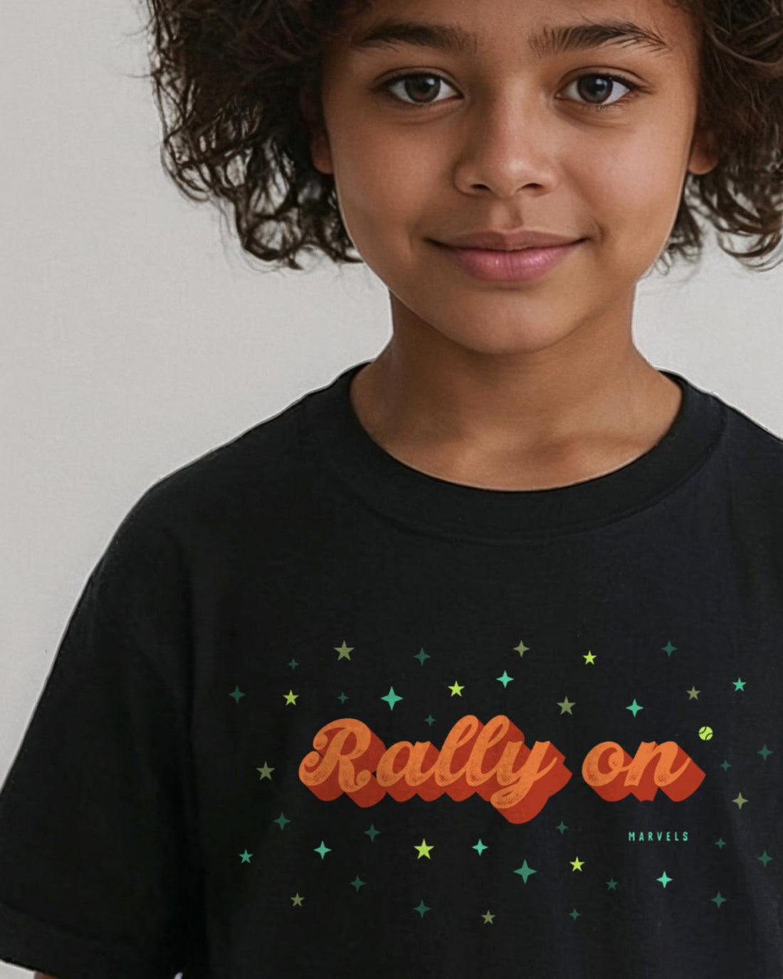 Child wearing a black tennis t-shirt with 'Rally On' text and star designs.