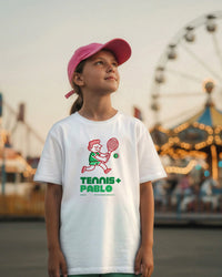 Child wearing a white t-shirt with a tennis-themed design at an amusement park.