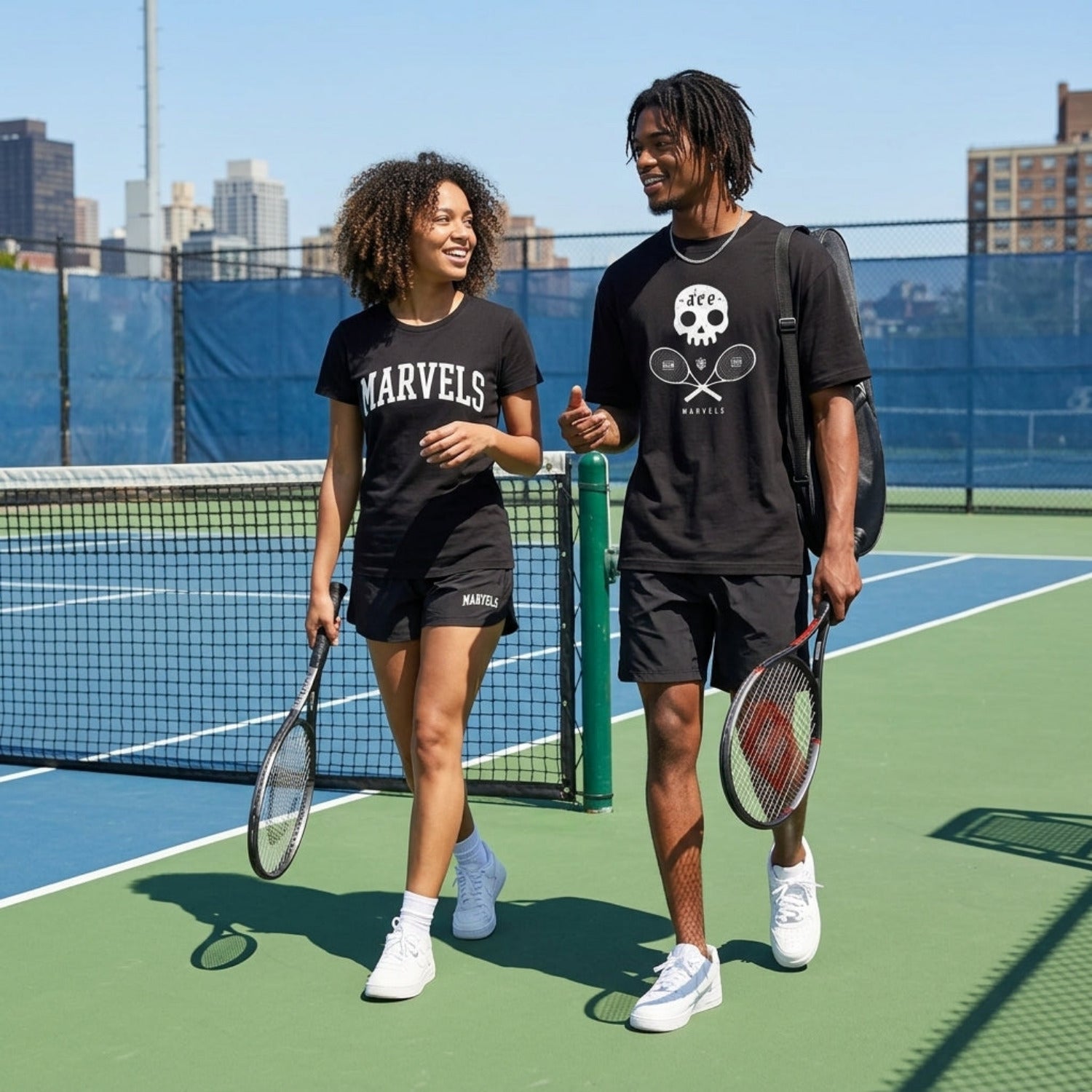 Two people on a tennis court holding tennis rackets, wearing black t-shirts with visible branding.
