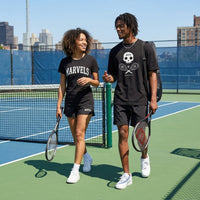 Two people on a tennis court holding tennis rackets, wearing black t-shirts with visible branding.