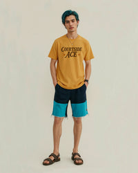 Person wearing a yellow gold t-shirt with 'Courtside Ace' text and black and blue shorts on a plain background