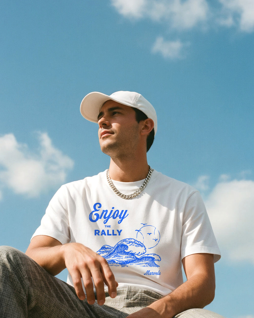 Man wearing a white t-shirt with tennis graphics against a blue sky.