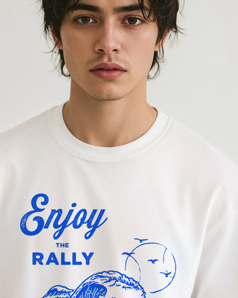 Person wearing a white t-shirt with blue 'Enjoy the Rally' text and graphics on a plain background