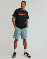 Man wearing a black t-shirt with text and light blue cargo shorts on a white background
