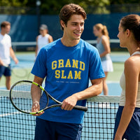 Man in blue 'Grand Slam' t-shirt holding a tennis racket on a tennis court with a woman.