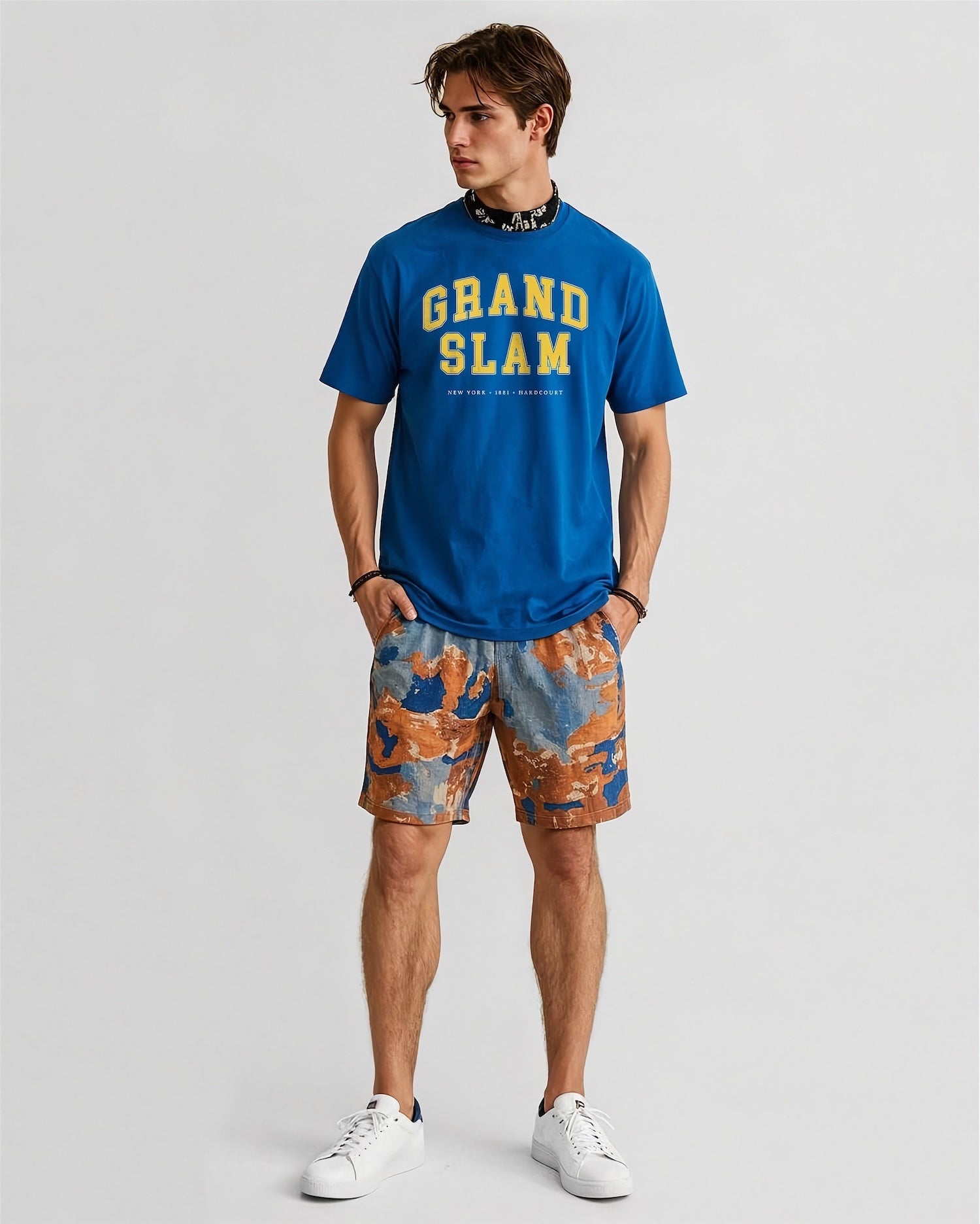 Man wearing a blue 'Grand Slam' t-shirt and patterned shorts on a light gray background