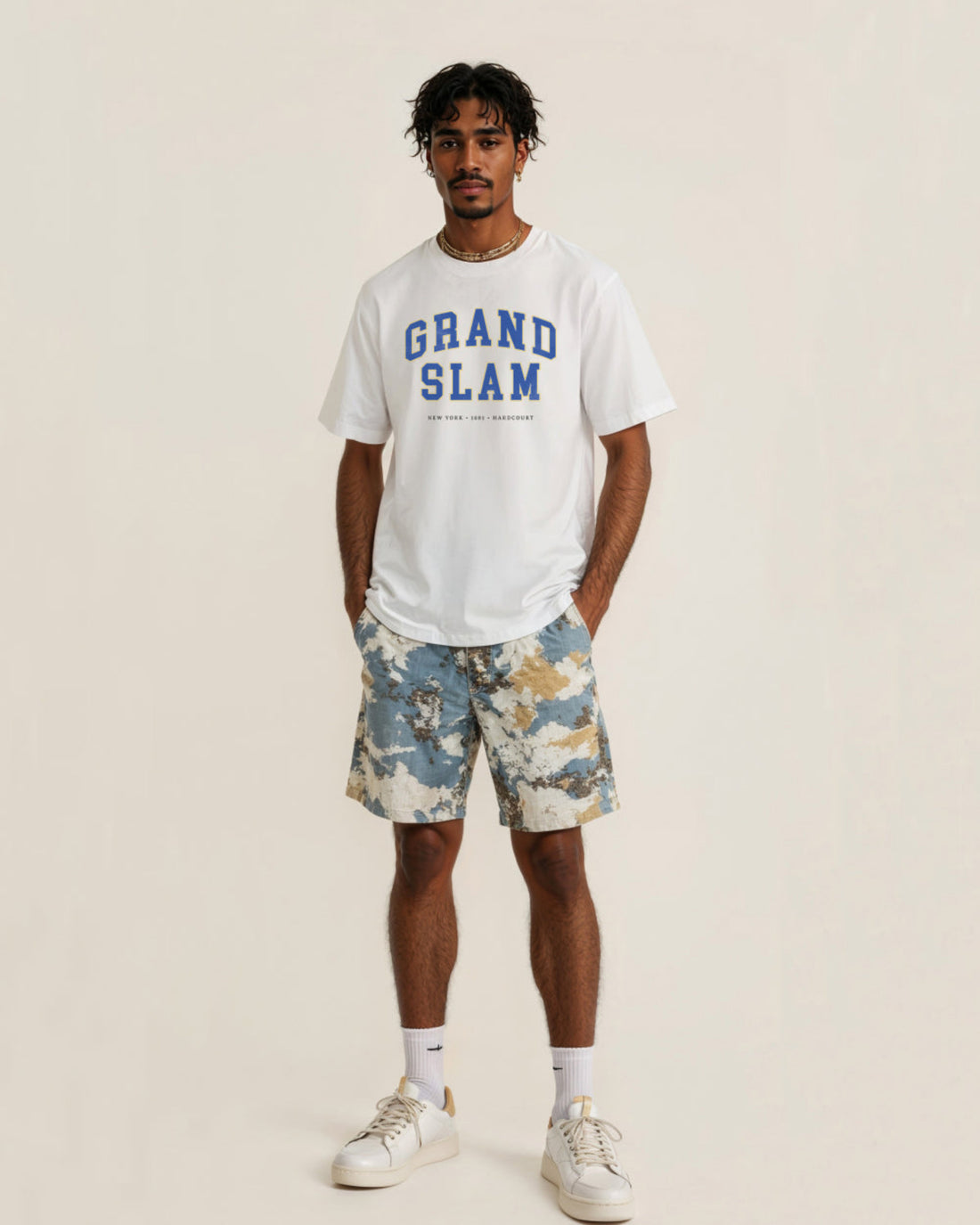 Man wearing a white 'Grand Slam' t-shirt and camouflage shorts on a beige background