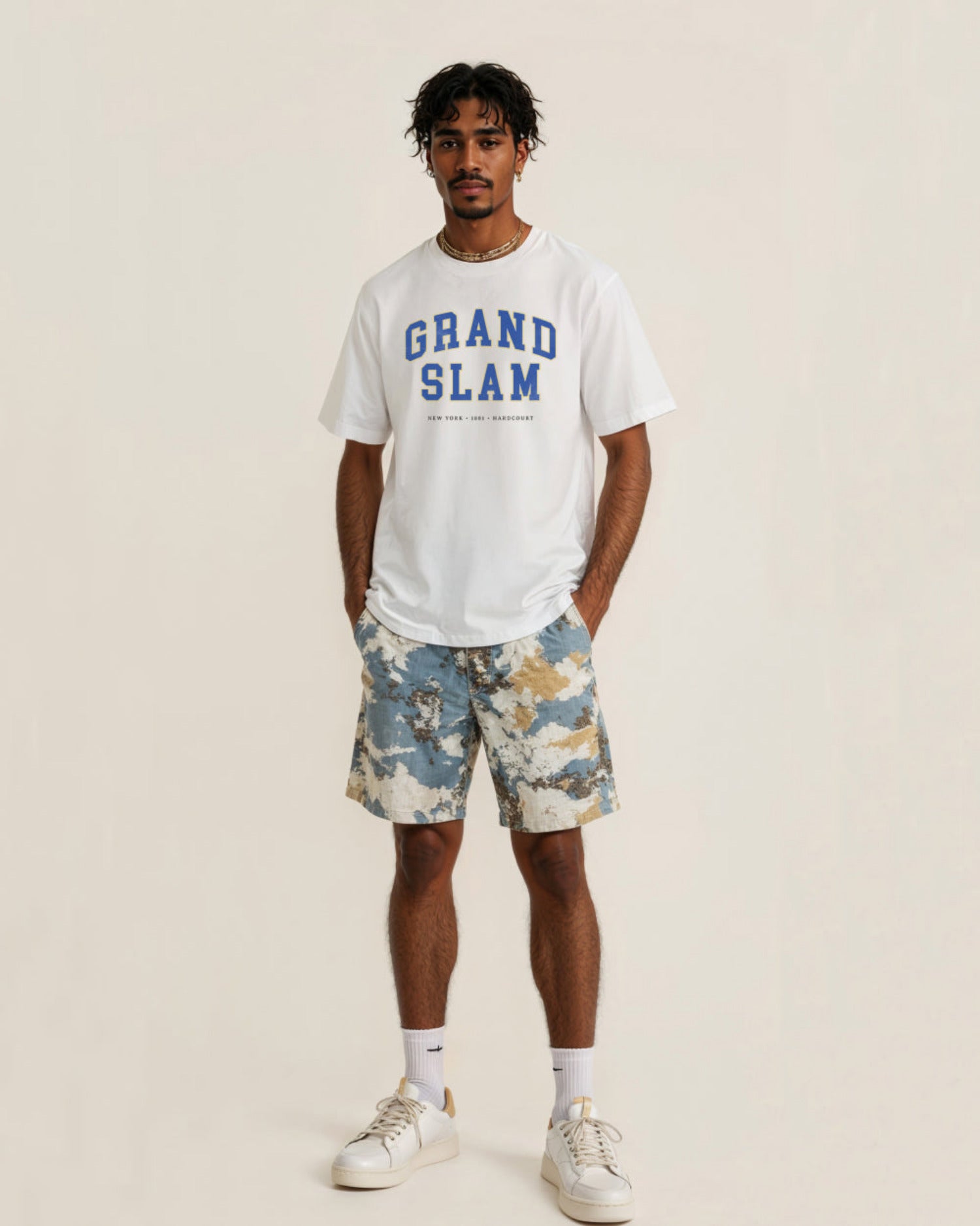 Man wearing a white 'Grand Slam' t-shirt and camouflage shorts on a beige background