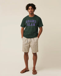 Man wearing a green 'Grand Slam' t-shirt and beige shorts on a plain background