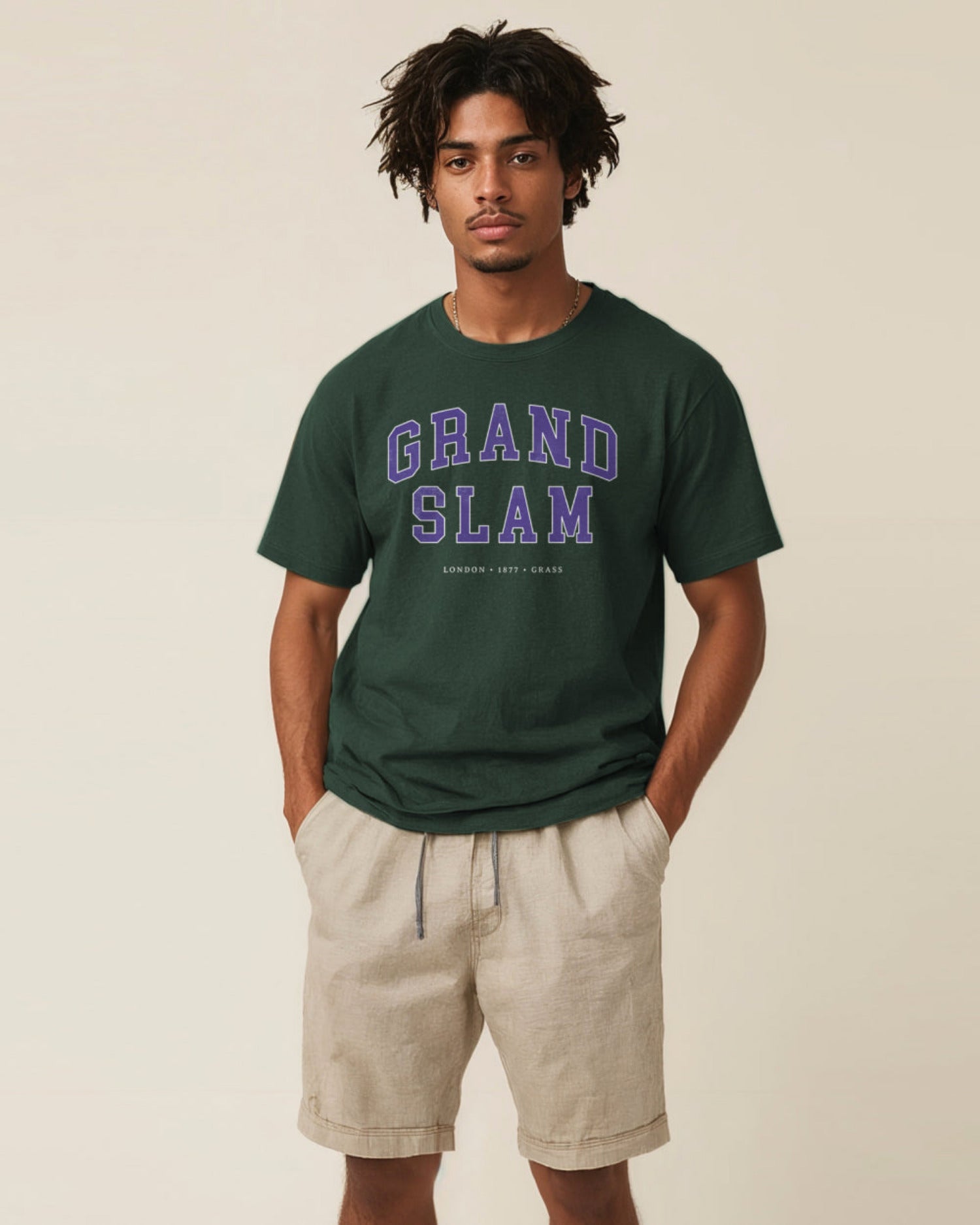 Man wearing a green 'Grand Slam' t-shirt and beige shorts on a beige background