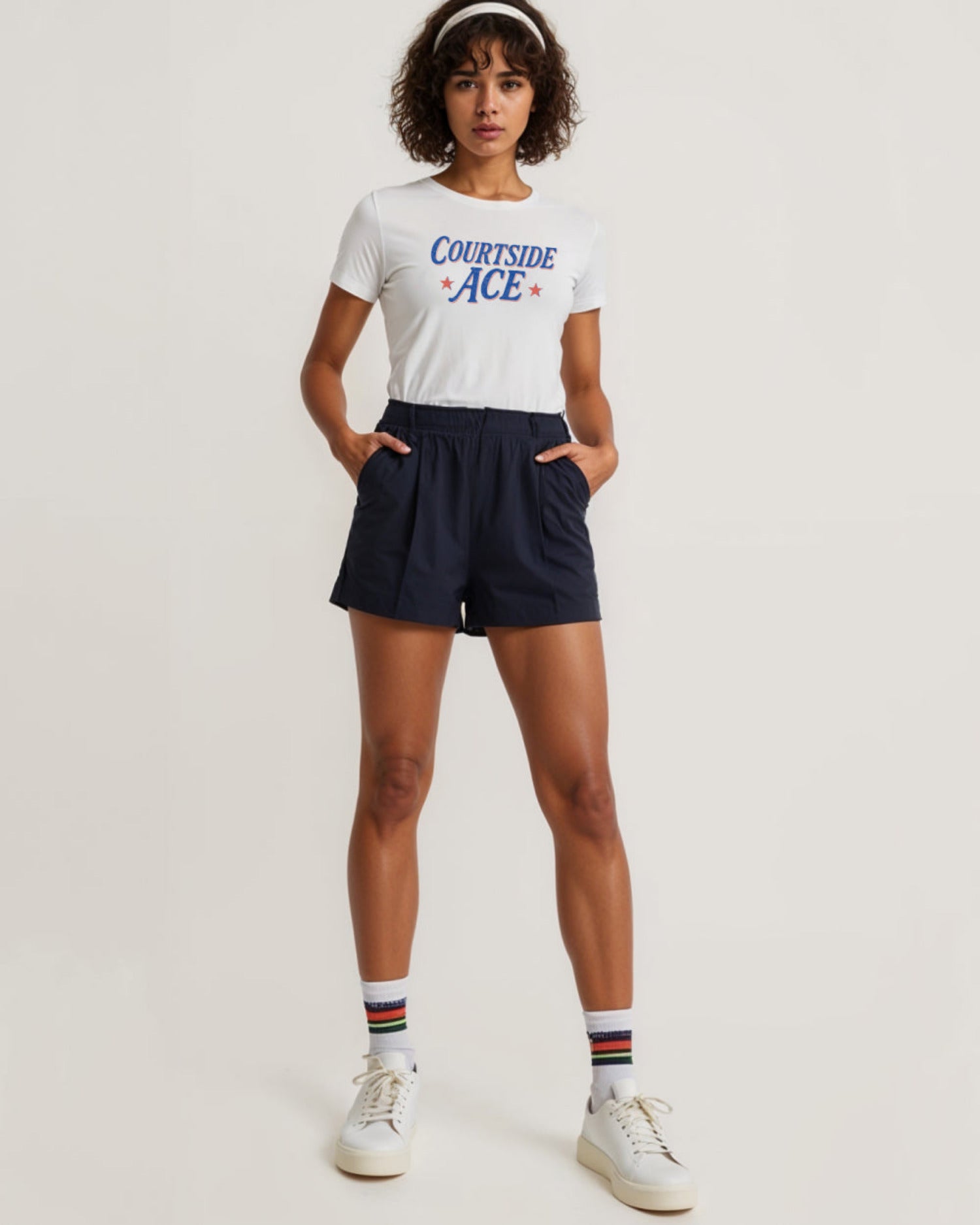 Woman wearing a white t-shirt with 'Courtside Ace' text and navy shorts on a light background
