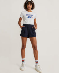Woman wearing a white t-shirt with 'Courtside Ace' text and navy shorts on a light background