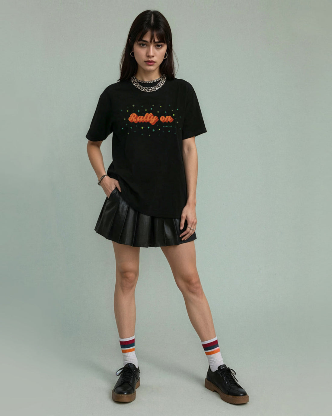 Person wearing a black tennis t-shirt with 'Rally On' text and a black pleated skirt on a plain background