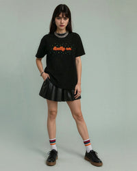 Person wearing a black tennis t-shirt with 'Rally On' text and a black pleated skirt on a plain background