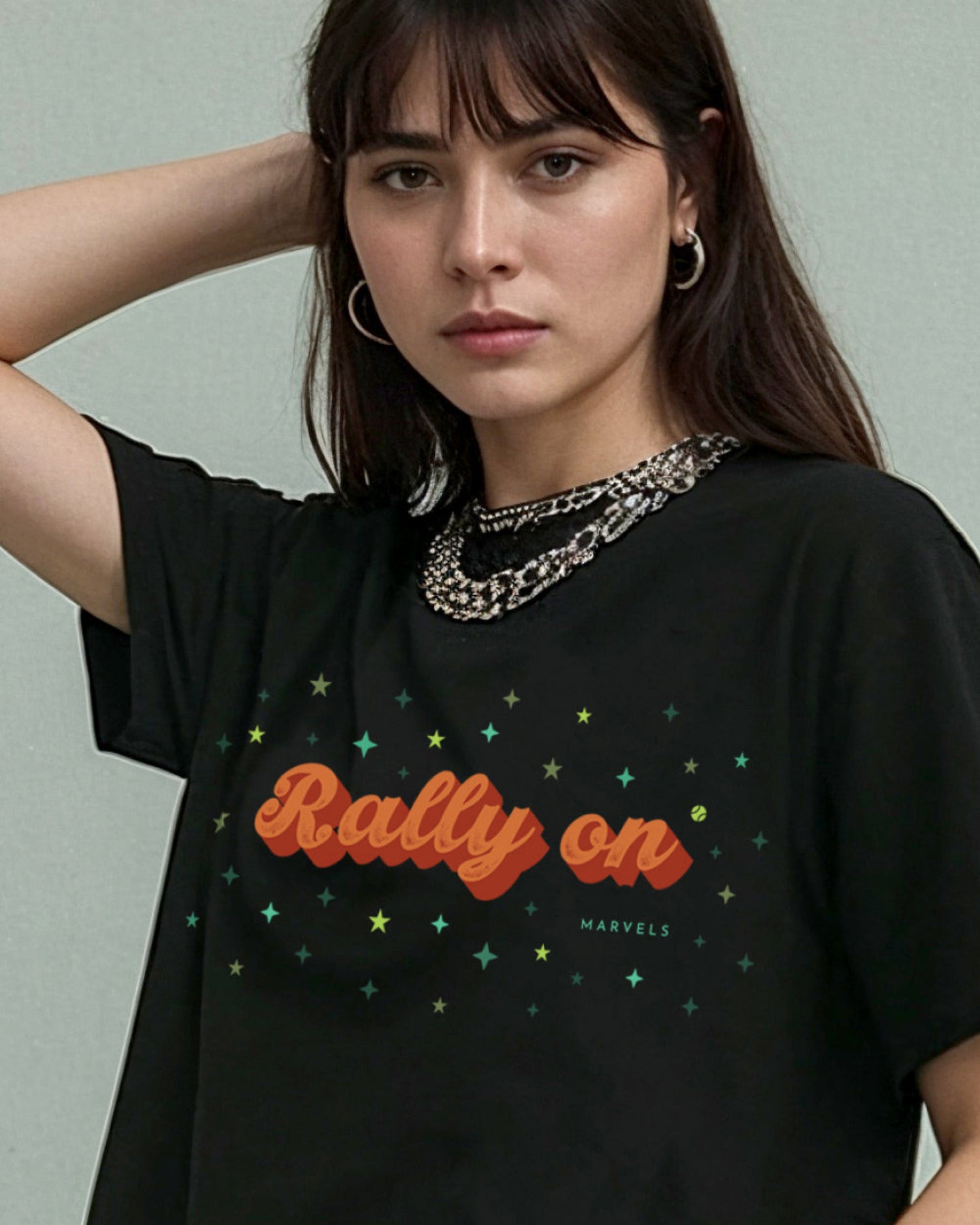 Woman wearing a black tennis t-shirt with 'Rally On' text and star designs, against a plain background.
