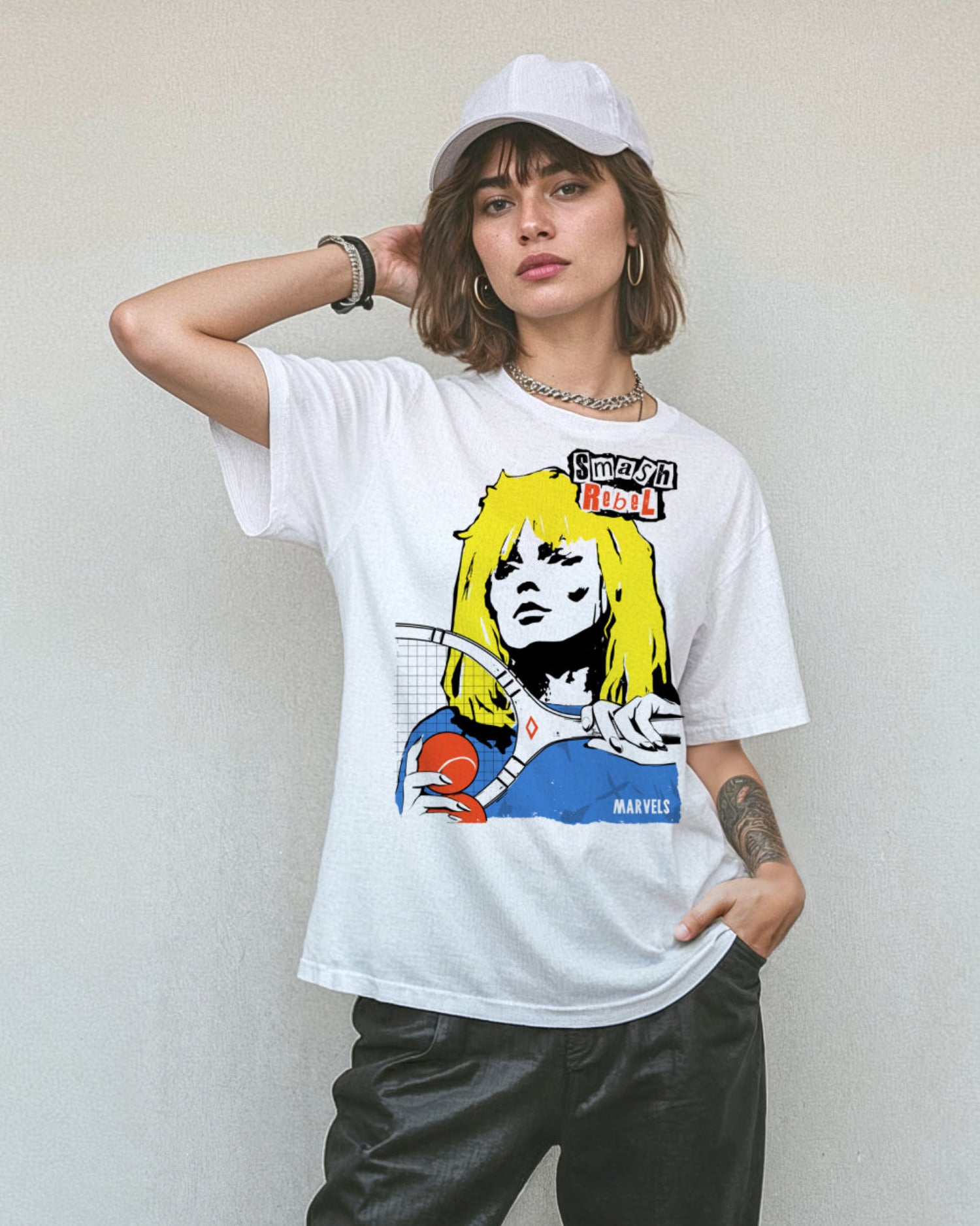 Model wearing black pants, a cap and a white t-shirt with a tennis-themed graphic that reads, 'Smash Rebel'.