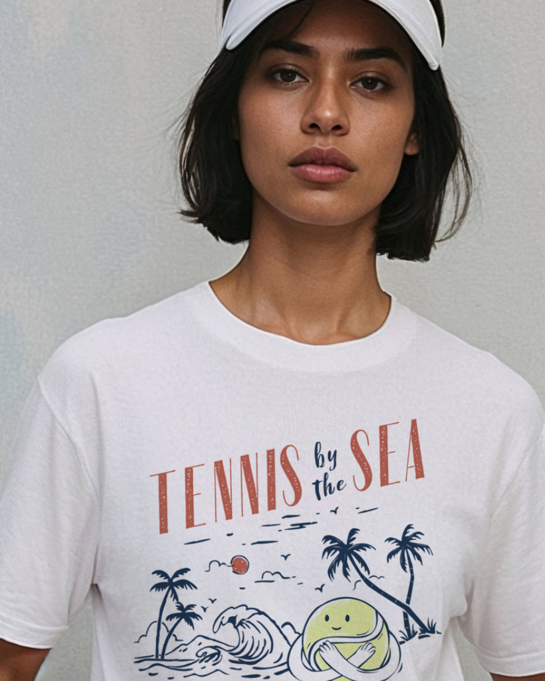 Person wearing a white t-shirt with a graphic that reads 'Tennis by the Sea'