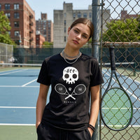 Person wearing a black t-shirt with a skull and tennis rackets design on a tennis court.