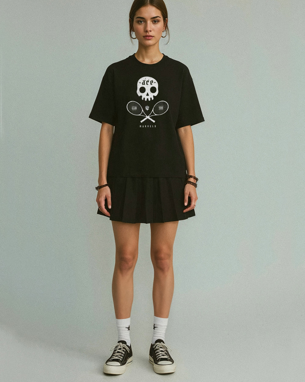 Woman wearing a black t-shirt with a skull and crossed tennis rackets design and a black skirt on a plain background