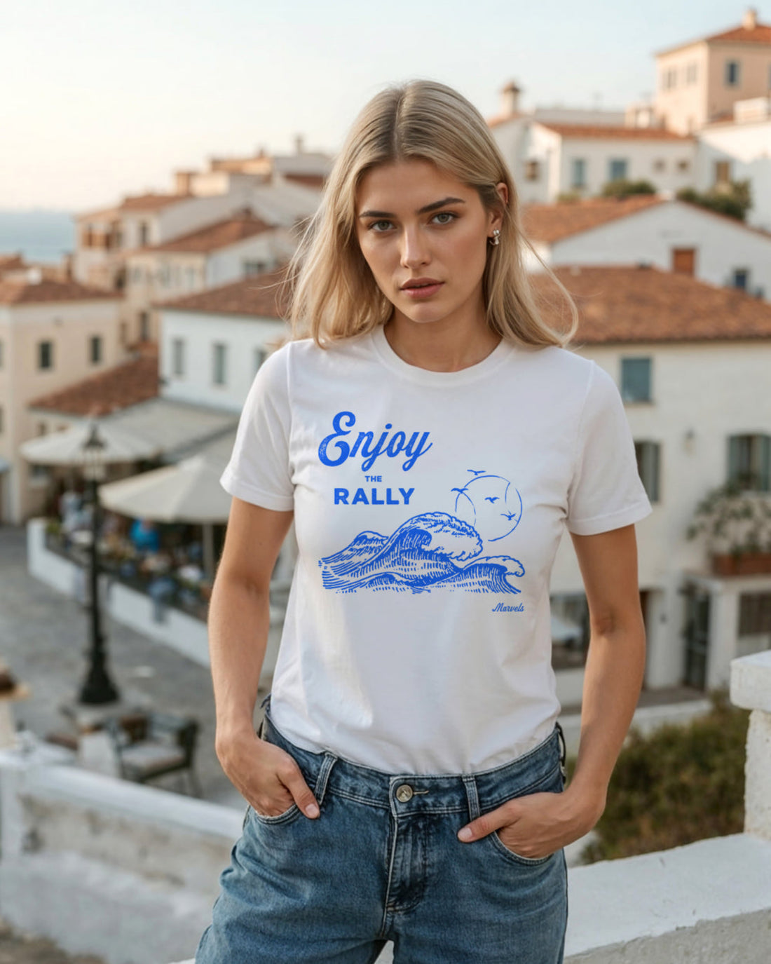 Woman wearing a white t-shirt with blue 'Enjoy the Rally' graphics and text, standing in a seaside setting.